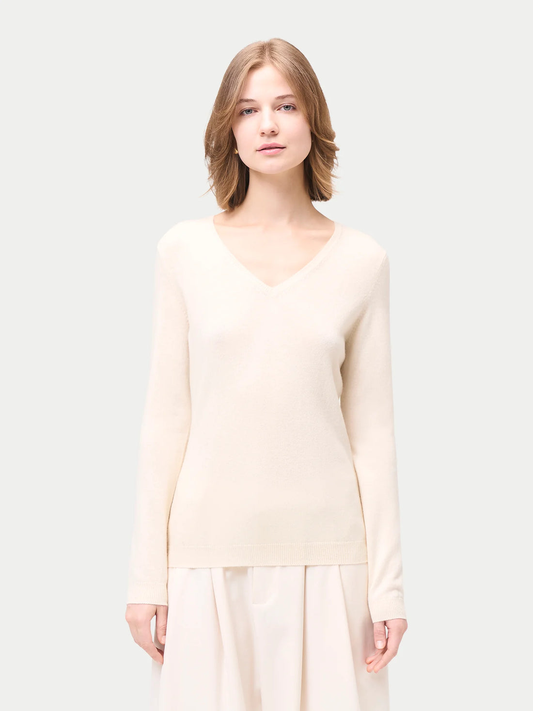 Woman wearing a light-colored sweater and pants on a white background